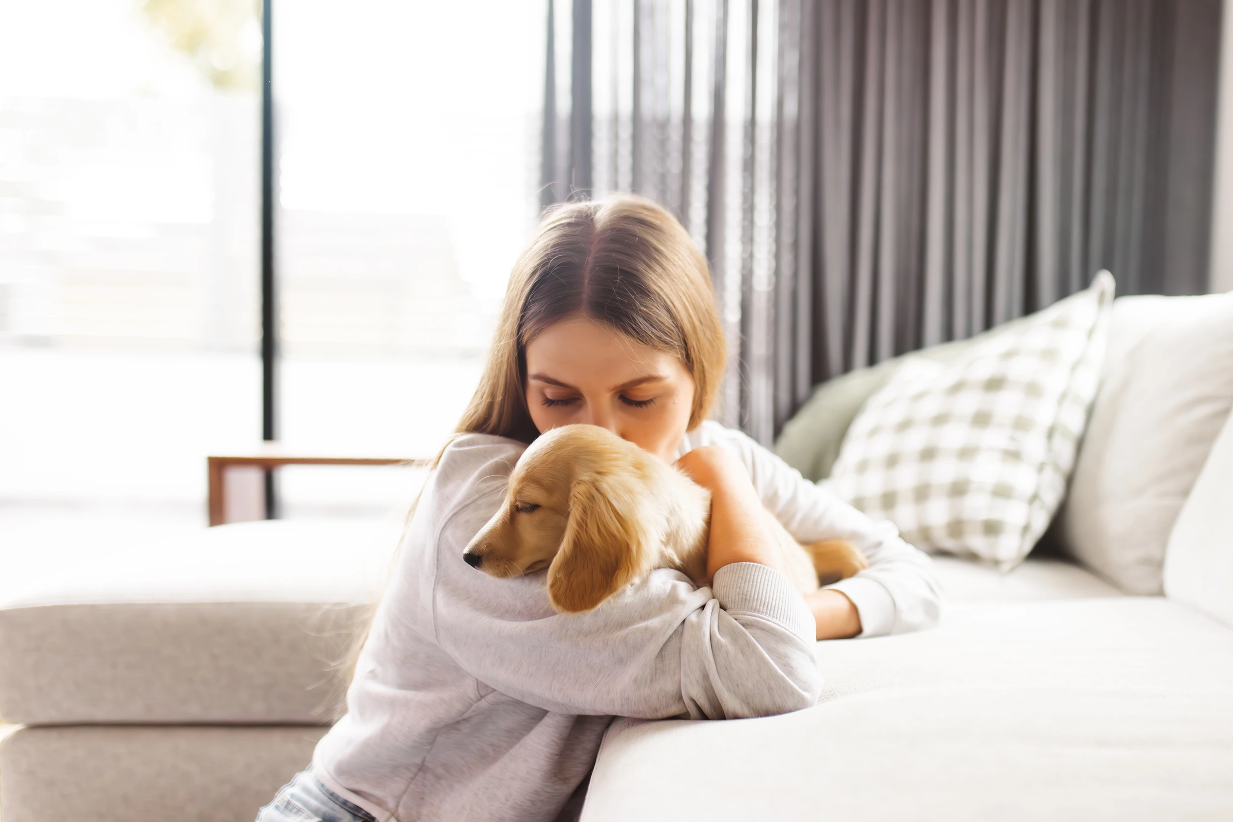 A woman cuddles a dachshund puppy on a light-colored sofa during a cosy family and puppy photoshoot in Melbourne