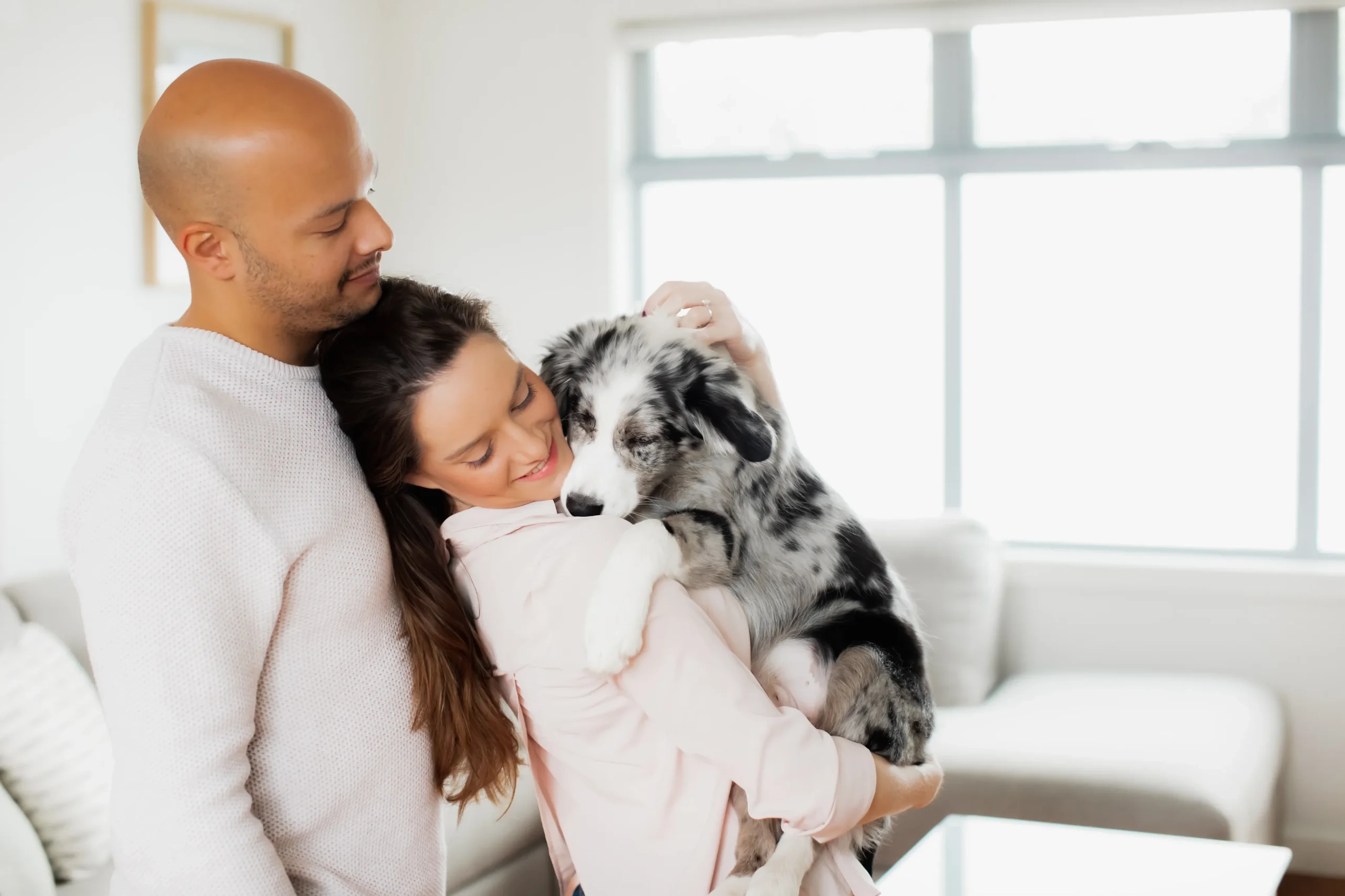 A couple joyfully holds their puppy during a candid and natural in-home professional puppy photoshoot